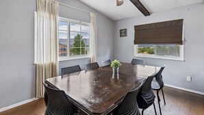 Une salle à manger avec une grande table, des chaises, un ventilateur de plafond et une vue sur l’extérieur.