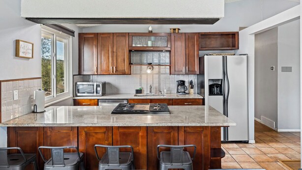 Une cuisine moderne avec des meubles en bois, un îlot central doté de tabourets, un réfrigérateur et un four à micro-ondes.
