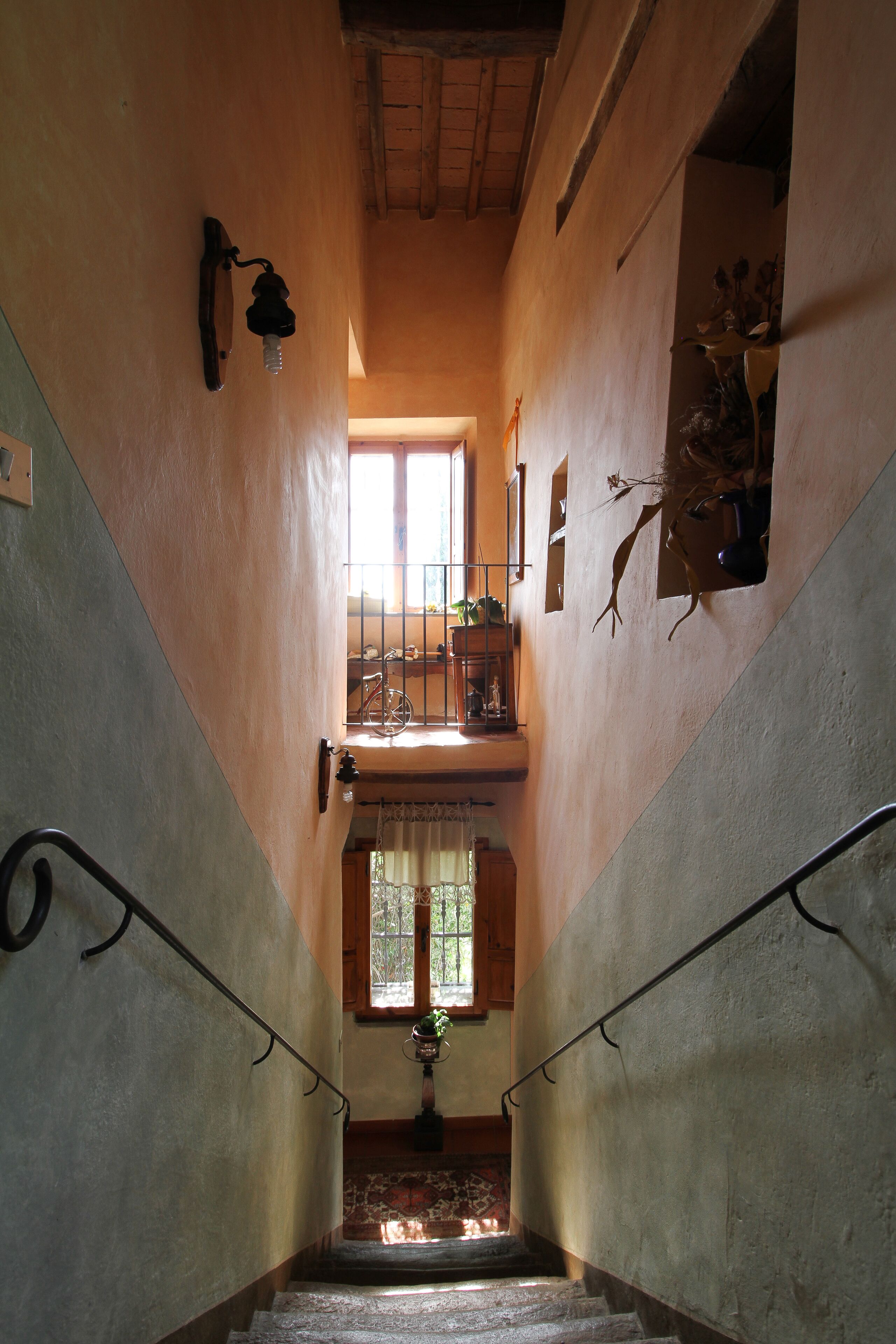 A staircase with a wooden handrail, a small balcony with a railing, and a window with curtains.