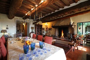 Ein Essbereich mit großem Tisch, gedecktem für eine Mahlzeit, Kamin und gemütlicher Sitzecke.