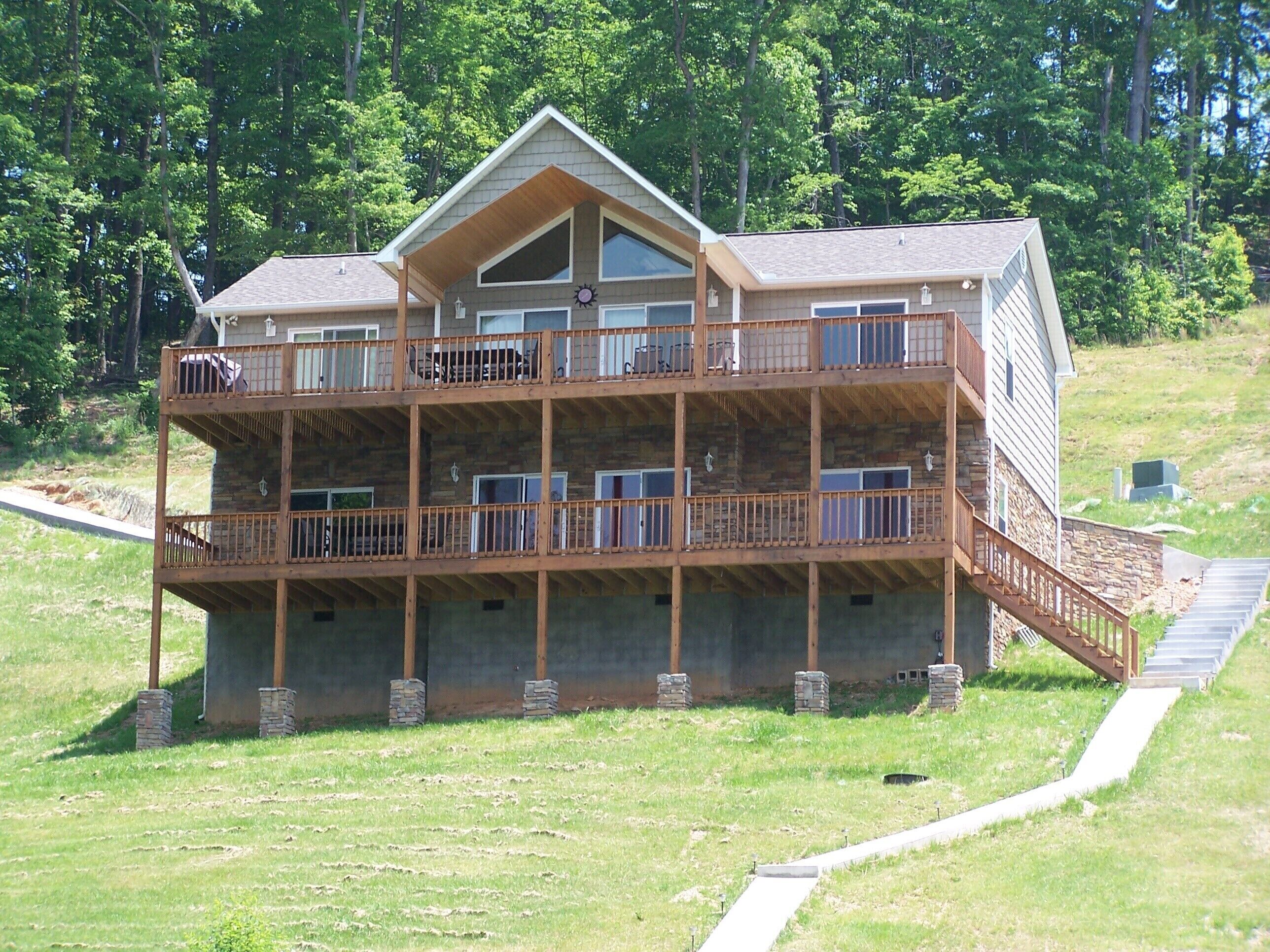 A multi-story wooden cabin with balconies, a stone foundation, and a grassy yard.