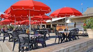 An outdoor patio area with multiple tables and chairs, red umbrellas, and a barbecue grill. - Villa; 5 minute walk to Palmetto Dunes Beach with a Great Golf Course View!! (Hilton Head Island)