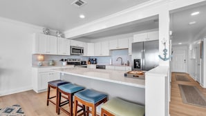 A modern kitchen with white cabinetry, a central island with stools, and stainless steel appliances.