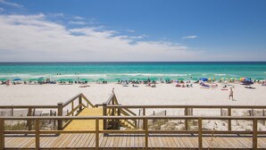 A beach with a wooden boardwalk leading to the water, umbrellas, and people relaxing on the sand.