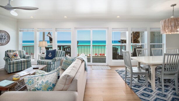 A spacious living room with a large window overlooking the ocean, furnished with a sofa, chairs, and a dining table.