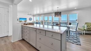 A spacious kitchen with a large island, a dining area with chairs, and a view of the outdoors through large windows.