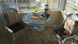 Eine verglaste Terrasse mit Korbstühlen und einem Tisch, mit einem Leuchtturm-Modell und einem Spielzeug für Kinder.