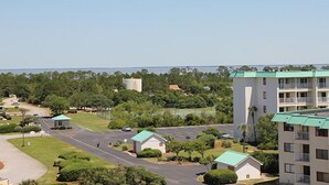 A multi-story hotel with a green roof, a parking lot, and a view of the surrounding greenery and water. - Inquiries are Beginning for Spring and Summer. Hear the Waves from  the Balcony. (Gulf Shores)