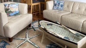 Ein Wohnzimmer mit einem beige farbenen Sofa, einem Couchtisch im Bootsdesign, einem Teppich mit Seesternen und einem Bild eines Leuchtturms.