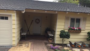 A house with a covered porch, two chairs, a door with a wreath, a window with flower boxes, and a garden with various plants and flowers. - Steps To Carmel Beach, in the golden rectangle. The perfect location! (Carmel-by-the-Sea)