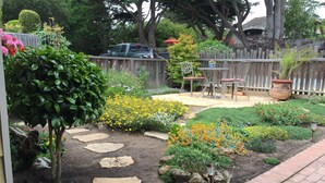 A garden with stepping stones, various flowering plants, a wooden fence, and a patio area with chairs and a table. - Steps To Carmel Beach, in the golden rectangle. The perfect location! (Carmel-by-the-Sea)