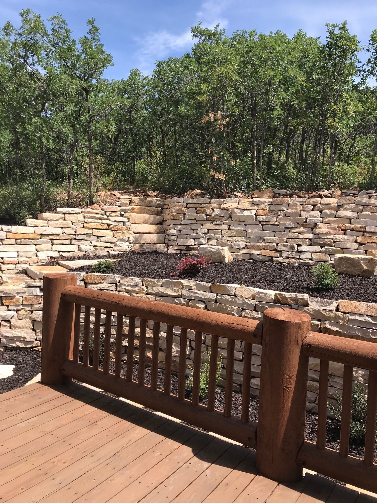 A wooden deck with a stone retaining wall and a bench.