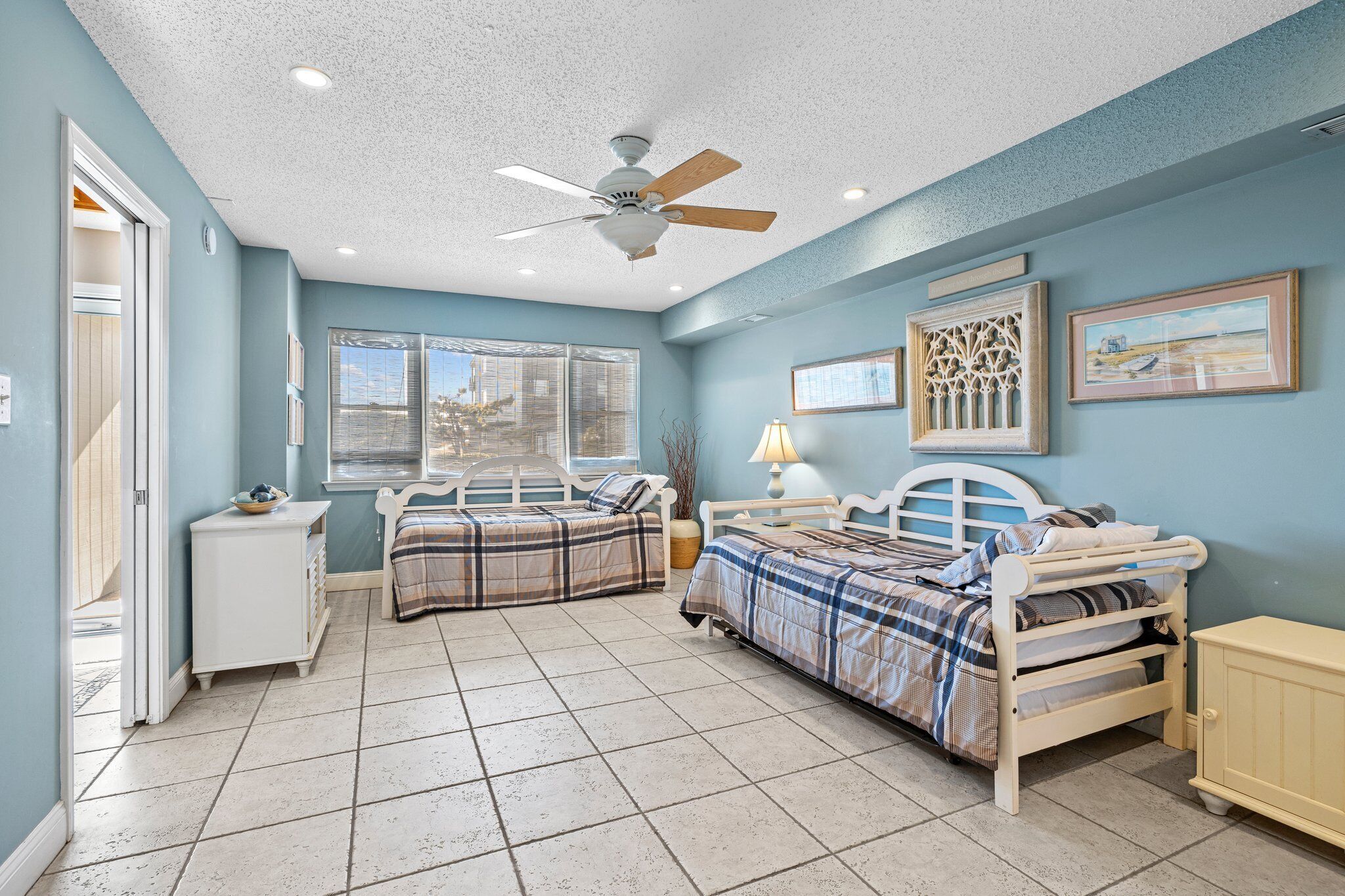 A bedroom with two beds, a ceiling fan, a window, and a door.