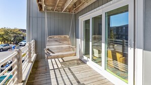 En träveranda med en gungstol, en glasdörr som leder ut till en balkong med gula stolar och utsikt över gatan och byggnaderna.