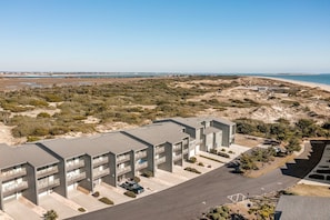 Ein modernes, mehrstöckiges Gebäude mit Balkonen, einem Parkplatz und Blick auf Strand und Meer.