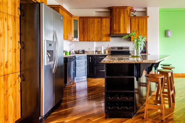 A kitchen with wooden cabinets, a stainless steel refrigerator, a built-in oven, and a granite countertop. - 2B / 2B IMPRESSIVE LAKE ARENAL, 3 POOLS, FULL KITCHEN (Tilaran)