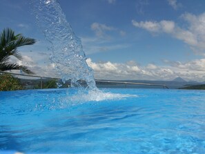 A pool with clear blue water and a palm tree on the left. - 2B / 2B IMPRESSIVE LAKE ARENAL, 3 POOLS, FULL KITCHEN (Tilaran)