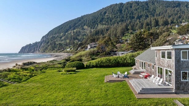 A coastal property with a patio area, a view of the ocean, and a hillside with trees and houses. - Manzanita Oregon beach house (Nehalem)