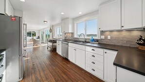 A modern kitchen with white cabinets, a stainless steel refrigerator, and a black countertop. - Manzanita Oregon beach house (Nehalem)