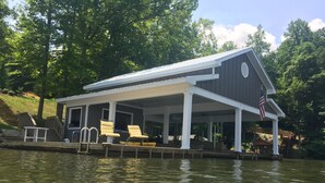 A covered dock with lounge chairs and an American flag. - Large Family Lakehouse w/ Dock, Deck, Patio, Views (Semora)