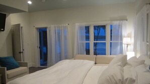 A bedroom with a large bed, a chair, and a view of the outdoors through the windows. - Large Family Lakehouse w/ Dock, Deck, Patio, Views (Semora)