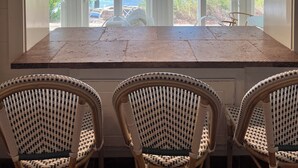 A kitchen with a large island, white cabinets, and a view of the lake. There are wicker chairs around the island. - Large Family Lakehouse w/ Dock, Deck, Patio, Views (Semora)