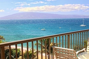 Enjoy the ocean views from this balcony, featuring a chair and table for relaxation, surrounded by palm trees.