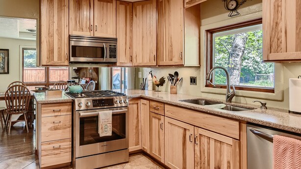 A kitchen with wooden cabinets, stainless steel appliances, a window with a view, and a rooster decoration.