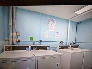 Un área de lavandería con dos lavadoras, una pared azul y algunos carteles de seguridad.