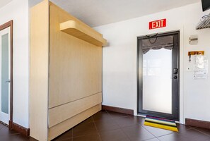 Un pasillo con estructura de madera, un letrero de salida, una puerta con cortina y suelo de baldosas.