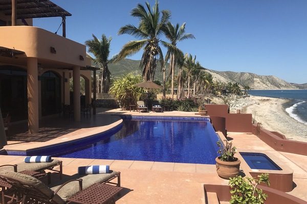 View of backyard patio w/ sunning chairs, infinity edge pool & large Jacuzzi.