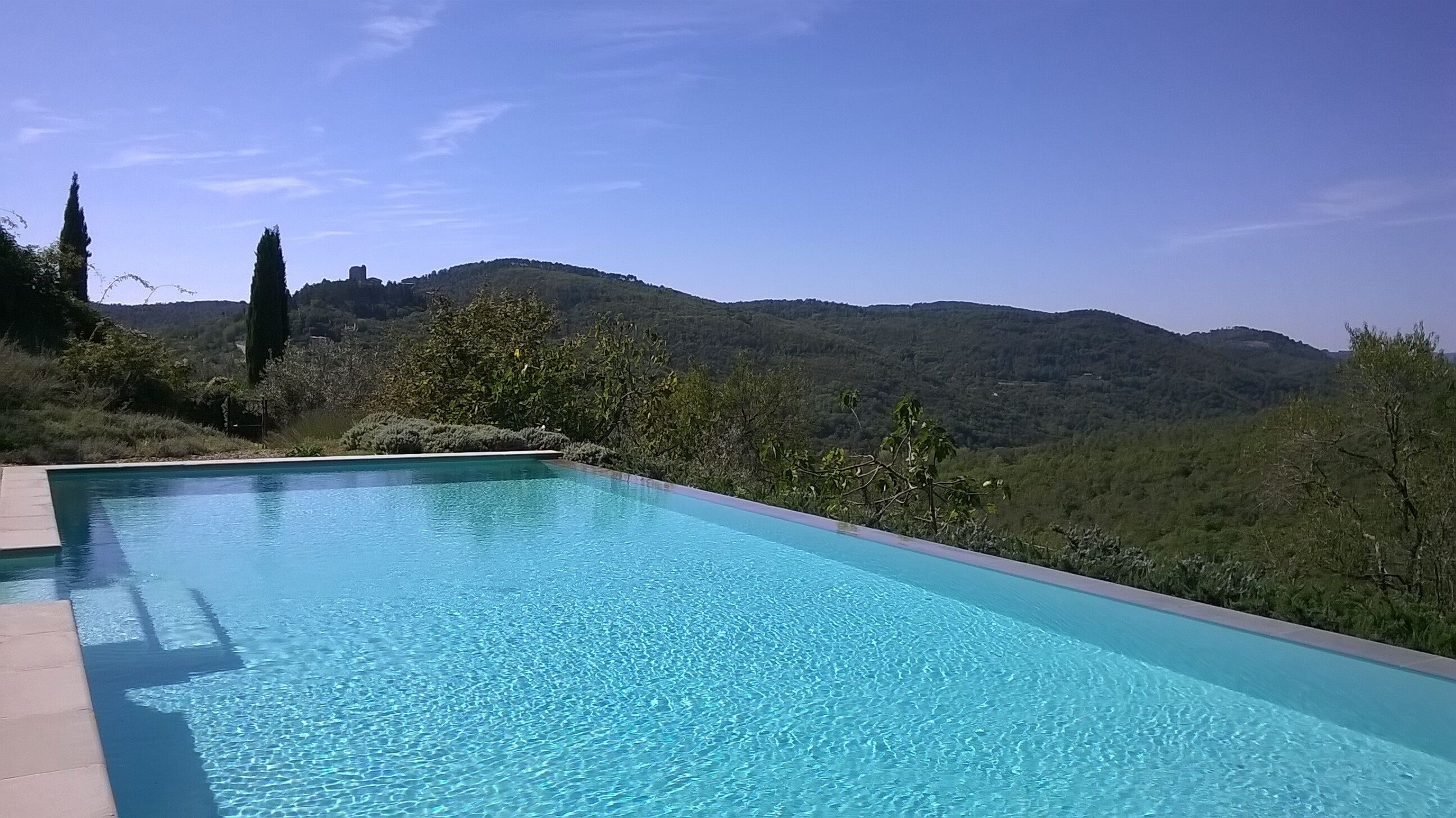 Una piscina a sfioro rettangolare con acqua cristallina, circondata da un solarium in pietra.
