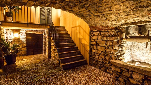 A stone-walled interior with a staircase leading to a second floor, a stone bench, and a small fountain. - Classy apartment with lake-view terrace and parking (Cernobbio)