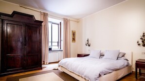 A bedroom with a large bed, a wardrobe, a window with curtains, a wall-mounted light fixture, and a radiator. - Classy apartment with lake-view terrace and parking (Cernobbio)