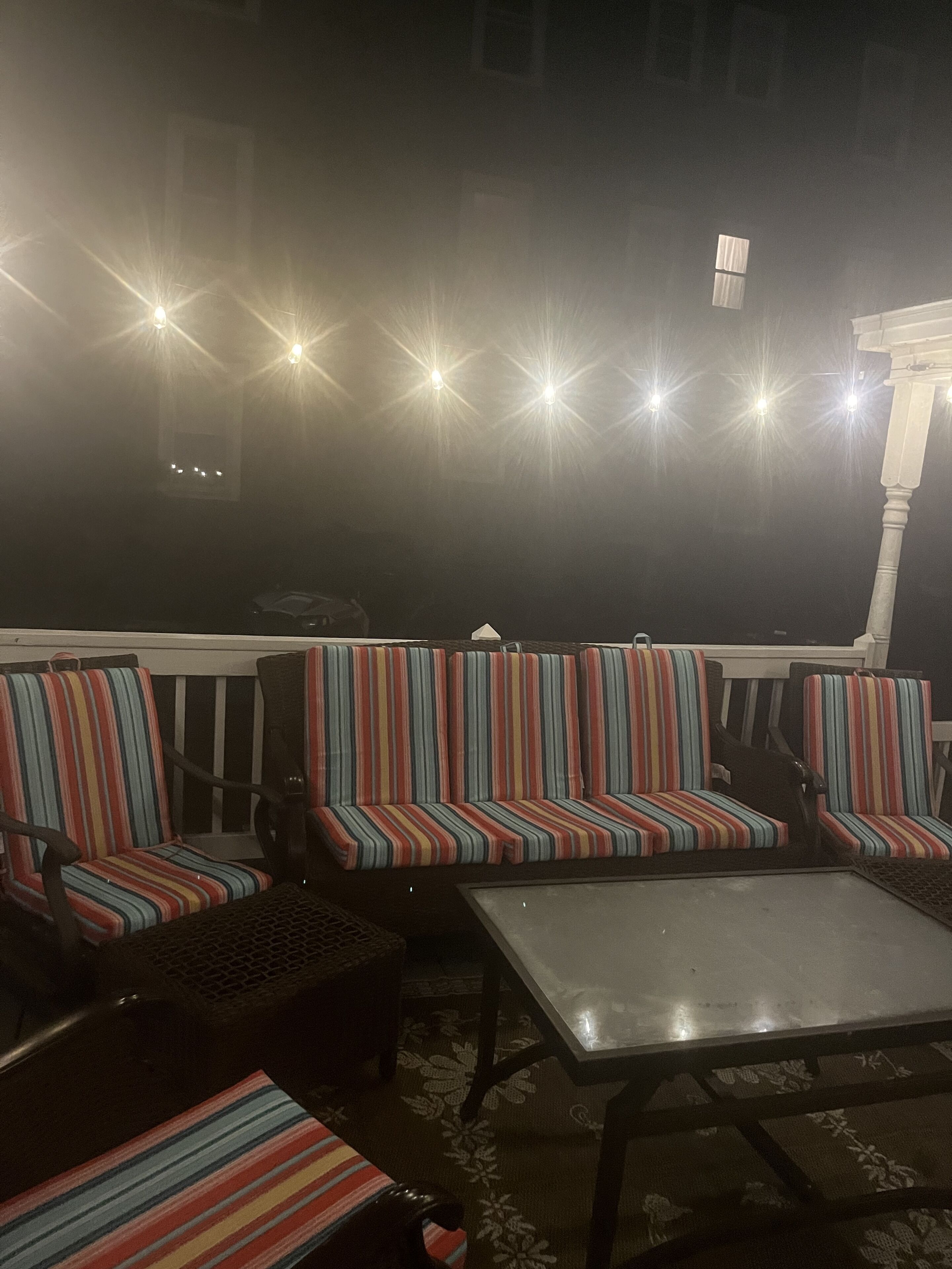 Ein schwach beleuchteter Außenbereich mit gestreiften Sofas und Sesseln, einem Metalltisch und einem gemusterten Teppich.
