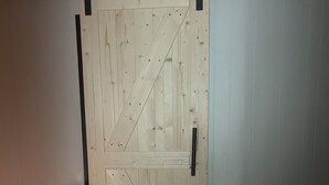A wooden sliding barn door with a black handle, set in a room with white walls and a wooden floor. - ATV and Snowmobile right from the house !!!! (Berlin)