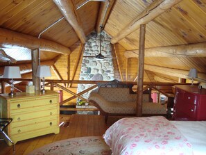 A cozy attic bedroom with a stone fireplace, wooden beams, and a bed with floral bedding. - Cozy log cabin on Beech Hill. (Mount Desert)