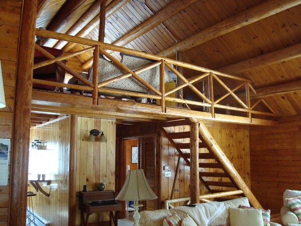 A wooden cabin interior with a loft bedroom, a staircase, and a dining area. - Cozy log cabin on Beech Hill. (Mount Desert)