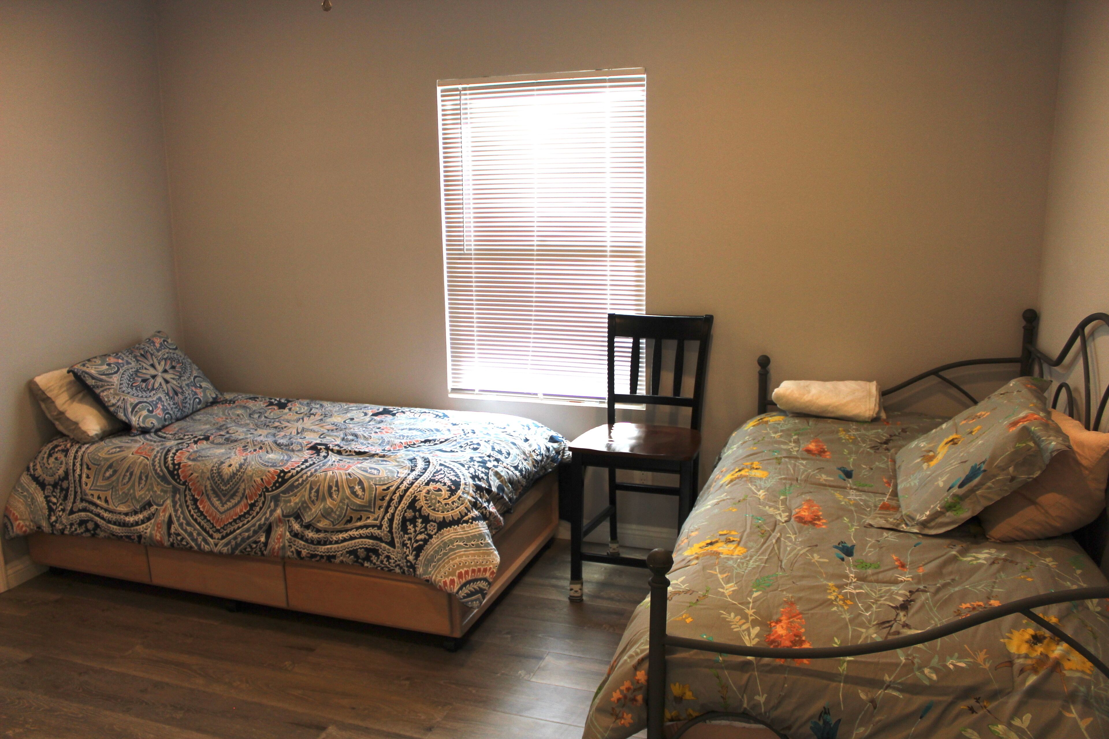 A bedroom with two single beds, a chair, and a window with blinds.