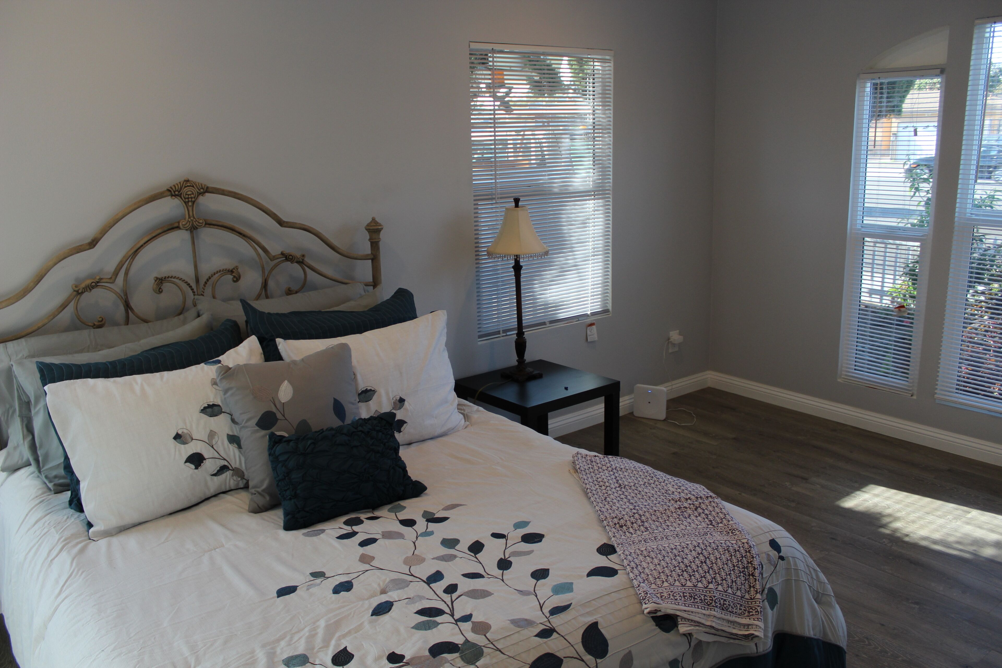 A bedroom with a bed, a nightstand, a lamp, and a window with blinds.