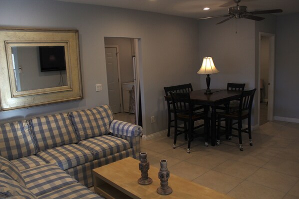 A living room with a sofa, a coffee table, a dining table with chairs, a ceiling fan, and a television mounted on the wall. - Vacation or executive rental in the heart of Orange County (Santa Ana)