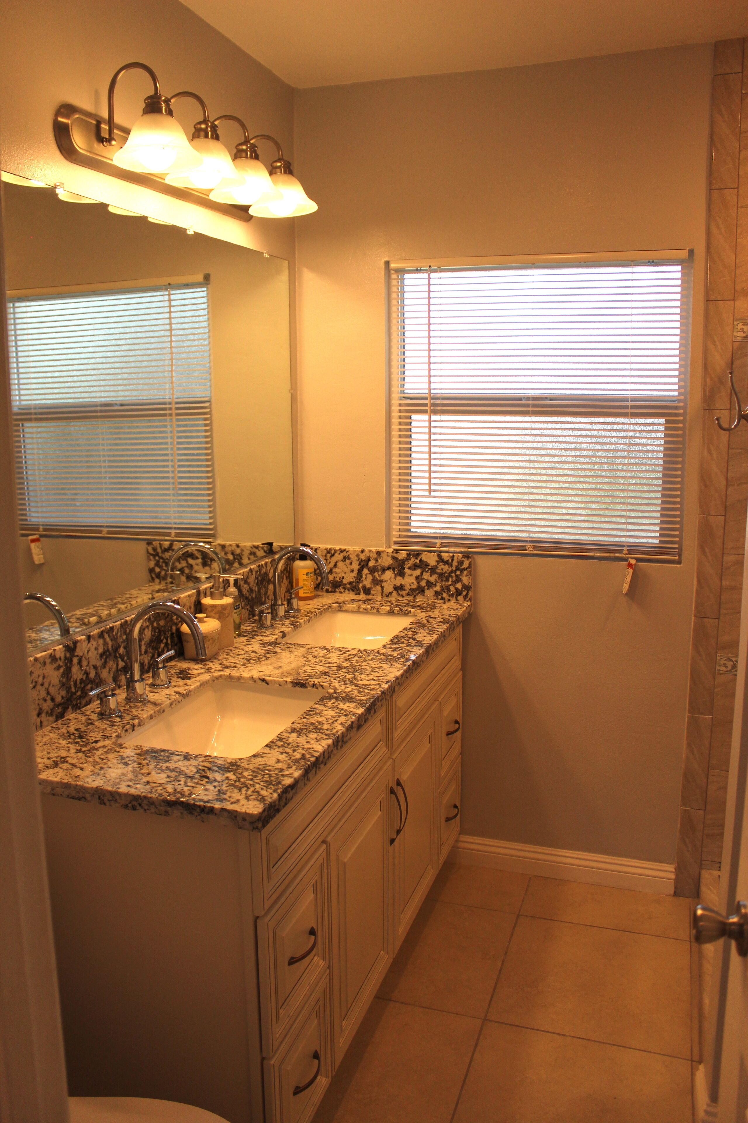 A bathroom with two sinks, a mirror, and a window with blinds.