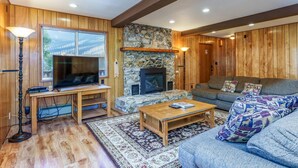A cozy living room with wooden walls, a stone fireplace, a television on a wooden stand, and a sofa with patterned cushions.