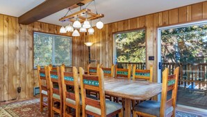 A wooden-paneled dining room with a large table and chairs, a patterned rug, and a view of the outdoors through large windows.