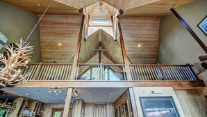Un intérieur spacieux avec un plafond haut, des poutres en bois, un balcon doté d’une balustrade et un lustre.