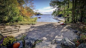 Un terrain de camping au bord du lac, avec un banc en bois, une tente et un bateau amarré près de l’eau.