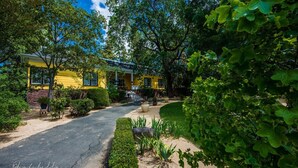 Una casa gialla con vialetto lastricato, immersa nel verde e alberi.