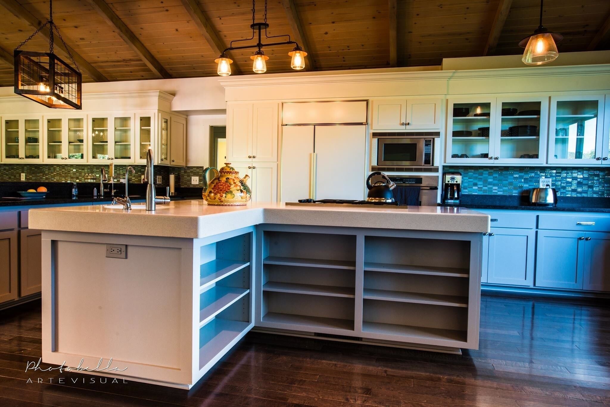 Una cocina moderna con armarios blancos, una isla grande con estantes integrados, un microondas y un hervidor.