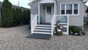 Une petite maison de plain-pied avec un porche et des marches menant à la porte d’entrée.
