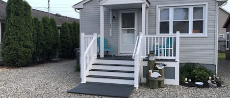 Een gelijkvloers huis met een veranda, een trap naar de ingang en een grindpad.